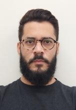 Márcio Medeiros Homem branco cabelo castanho com barba grande e bigode usa óculos e camisa preta